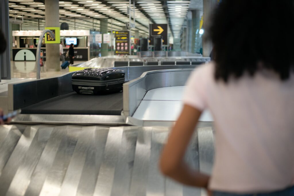 Kofferband am Flughafen und Frau die auf ihr Gepäck wartet